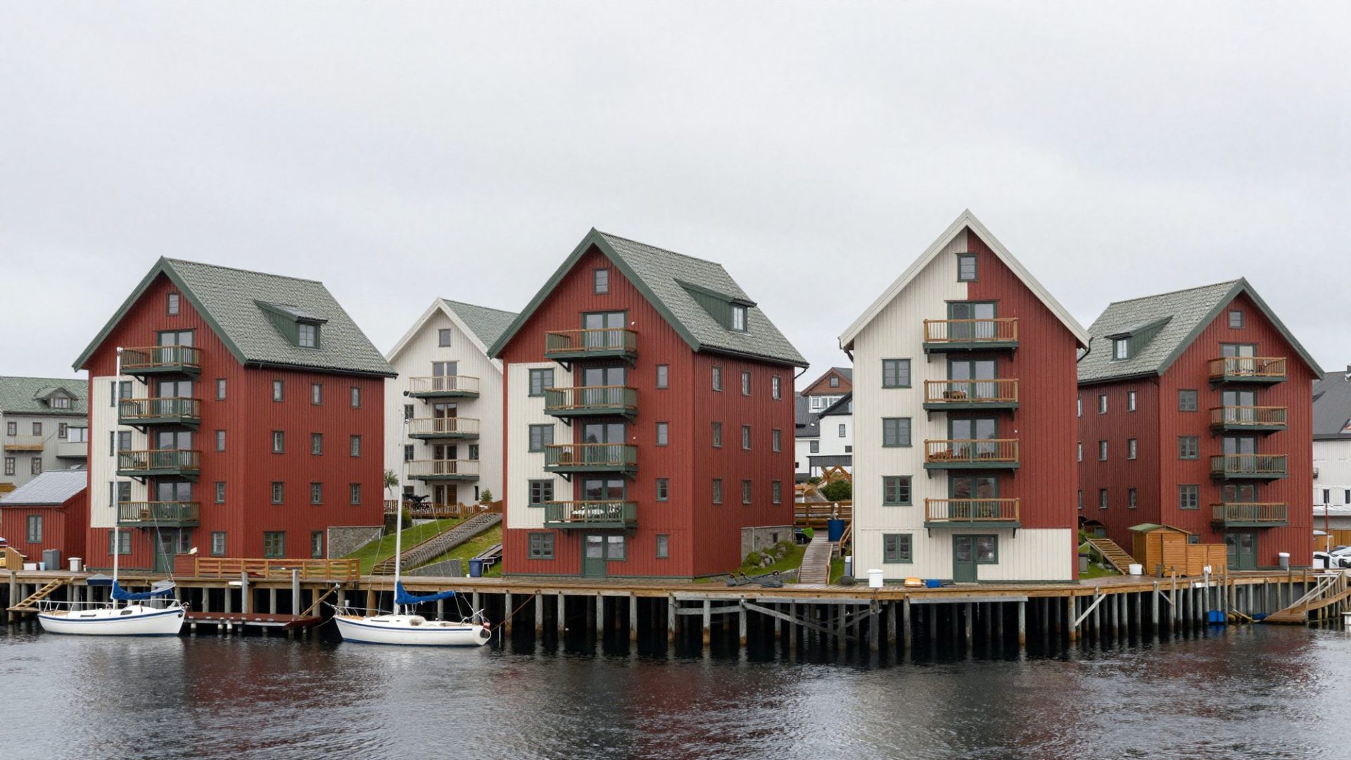 Four slim gabled apartment buildings in red ochre, white and green timber on a harbour quay.