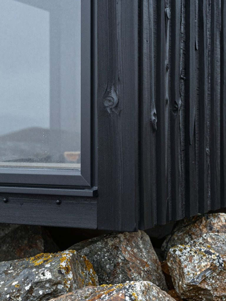 Charred timber cladding meeting a black window frame, with raindrops on the glass.