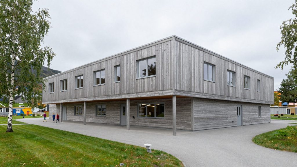 A two-storey school clad in silvery pine with a long covered walkway and birch trees.