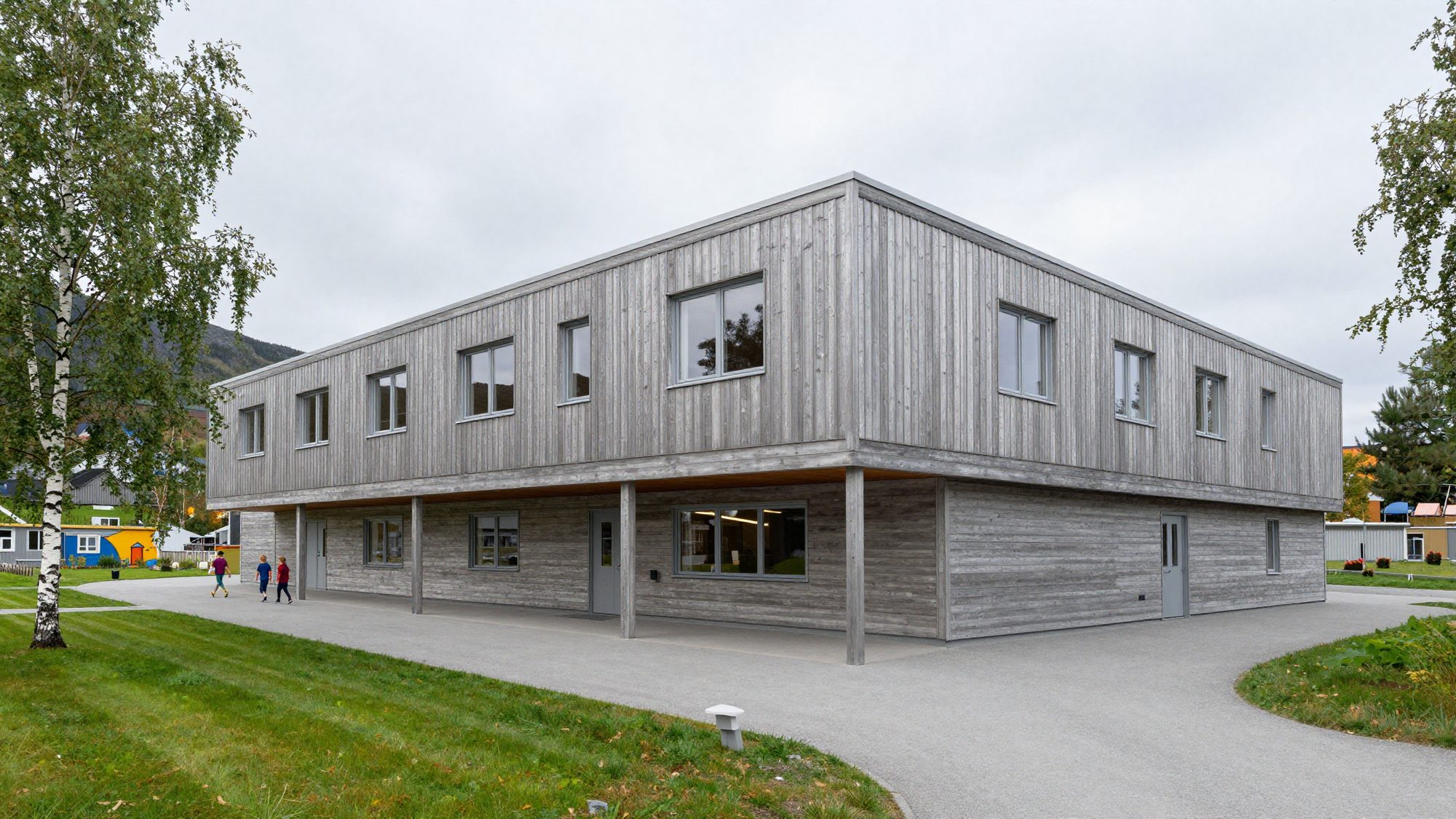 A two-storey school clad in silvery pine with a long covered walkway and birch trees.