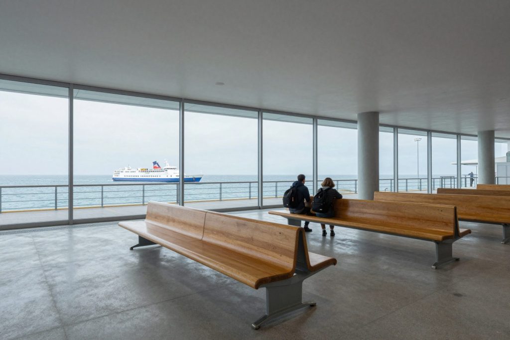 A concrete waiting hall with a long timber bench and full-height glass towards the sea.